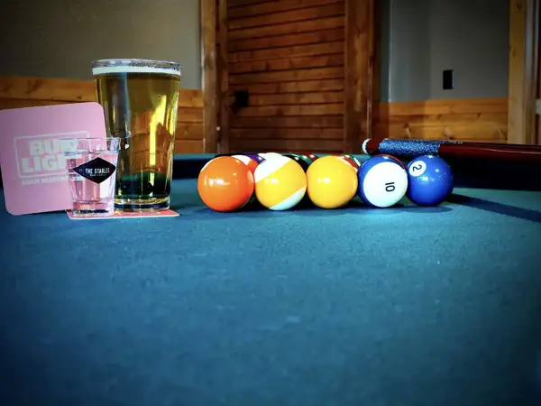A pint of beer and a pool table setup with balls. 